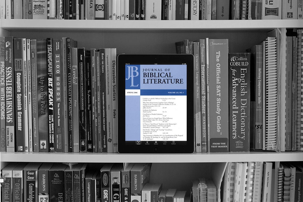 Journal of Biblical Literature on a tablet screen in the middle of a bookshelf of traditional reference books.