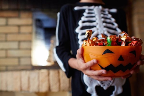 A skeleton-costumed child holding out a pumpkin bowl of Halloween candy