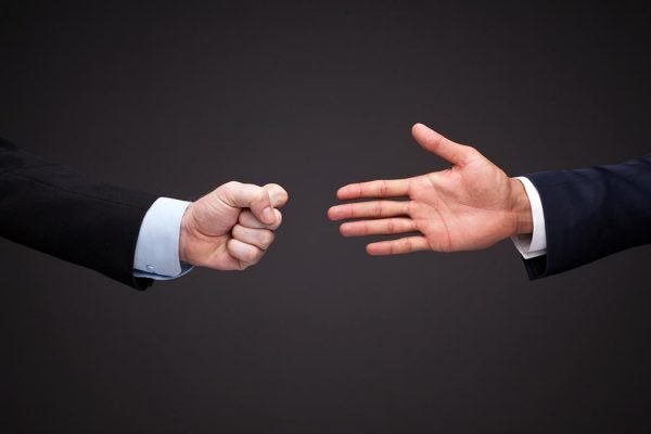 One hand outstretched for a handshake and on the opposite side a hand clenched in a fist