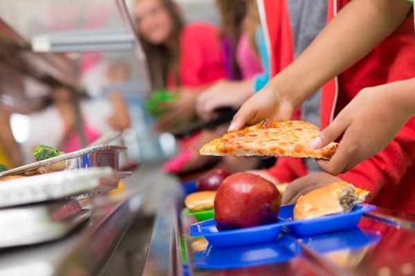 A student getting pizza to add to a burger and an apple from the school cafeteria line