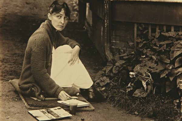 Black and white photograph of Georgia O'Keefe sitting on the ground and sketching