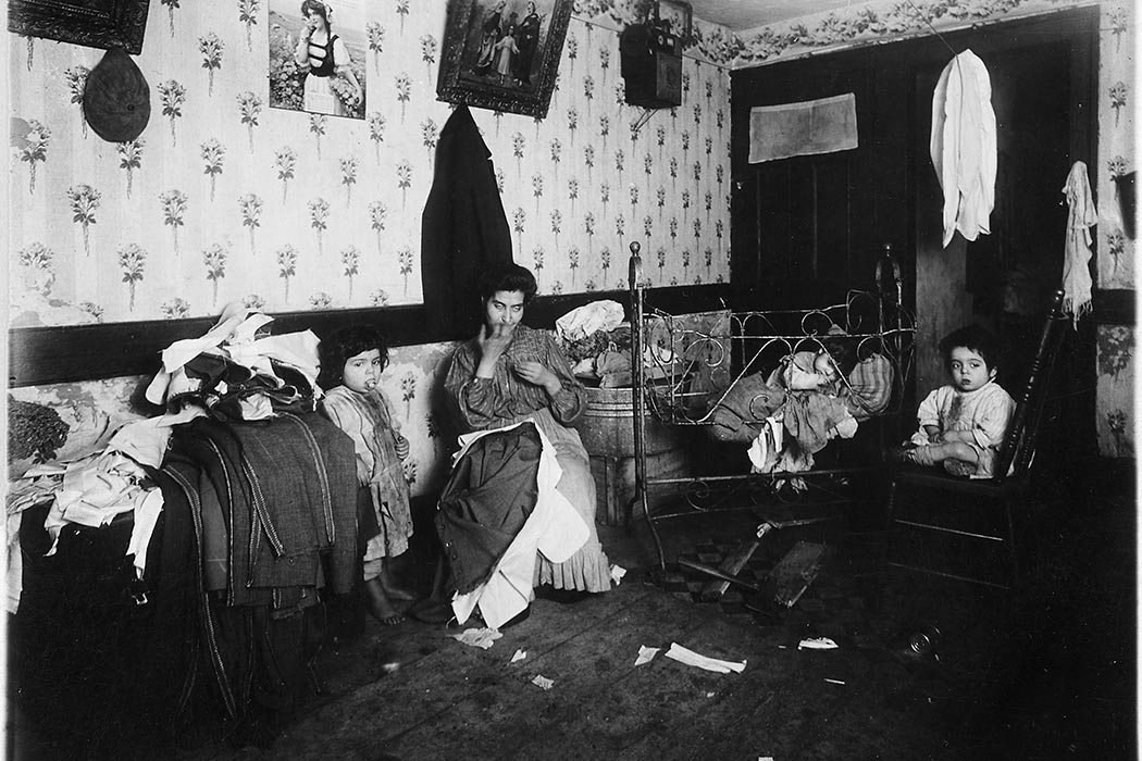 Older black and white photograph of a woman in the middle of a messy living room with three small children of various ages