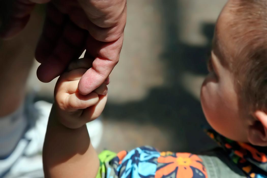 A baby holding the finger of a caretaker