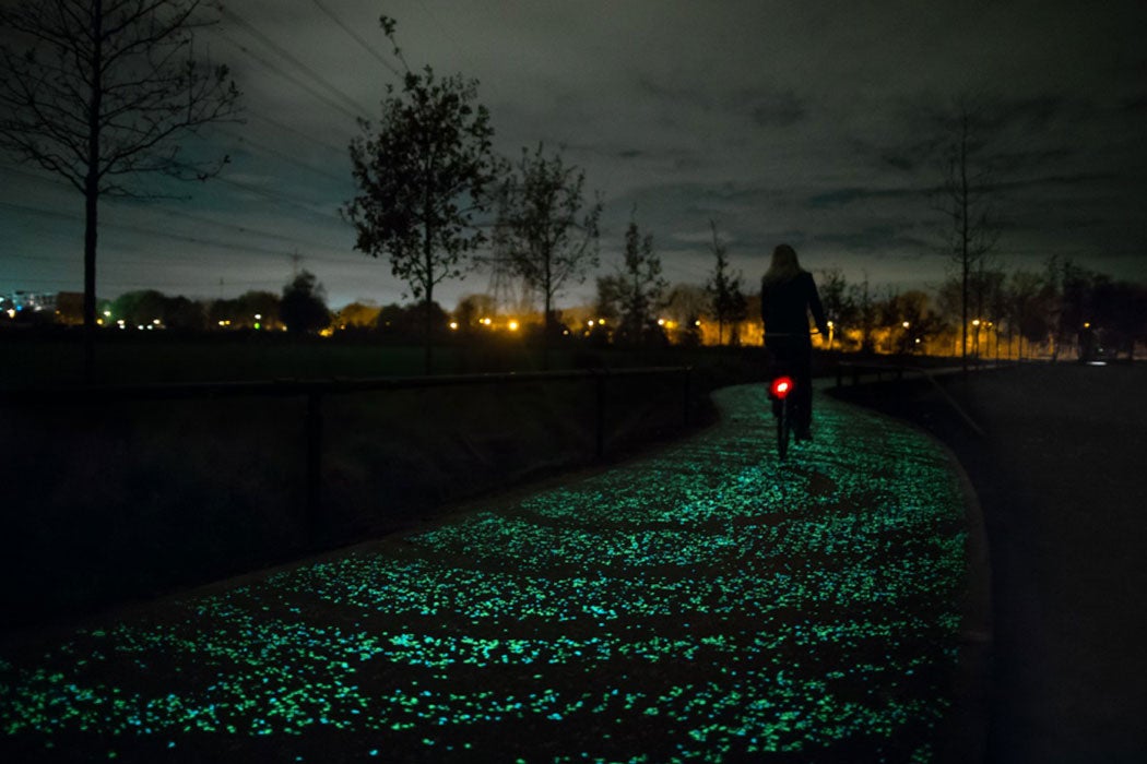 A lone biker rides on a glowing trail at night