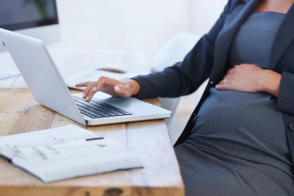 A pregnant woman works on a laptop