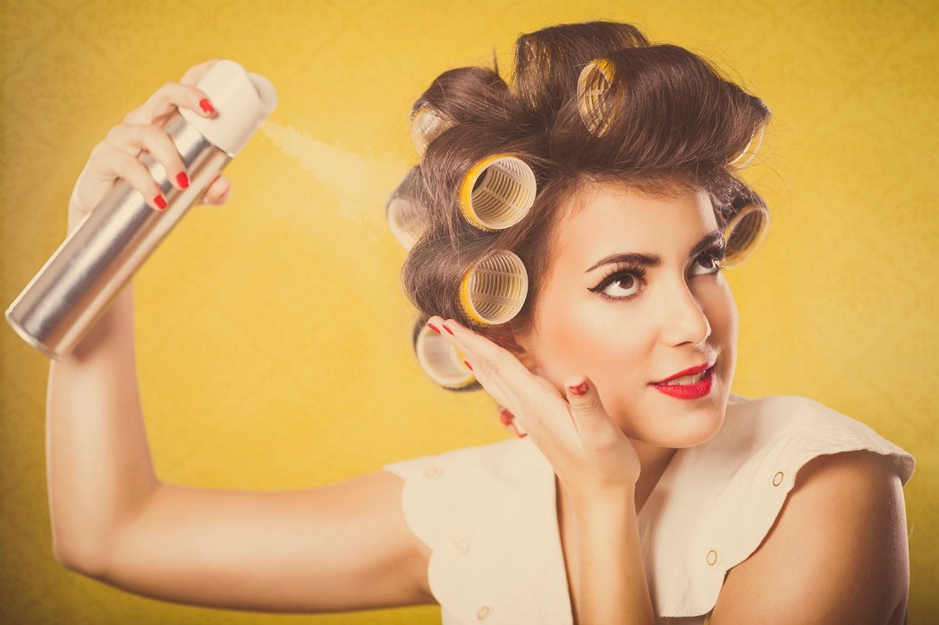 A woman with her hair in curlers spraying and holding the curlers in place
