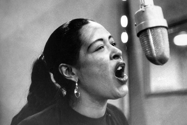 Billie Holliday singing into a studio mic in black and white