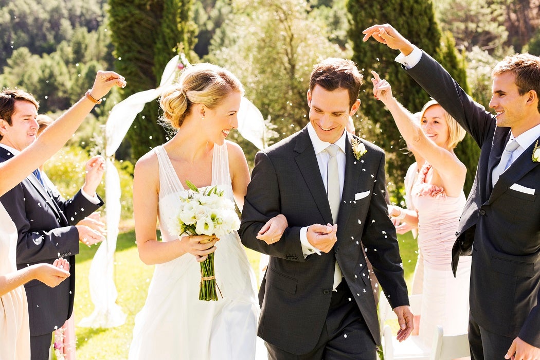 Happy couple walking while guests throwing confetti on them during wedding ceremony. Horizontal shot.