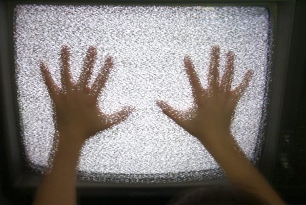 A child's hands pressed up against a static-filled television