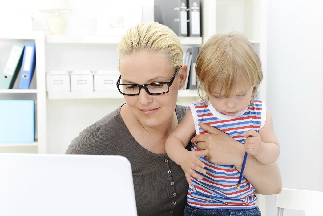 A mother working on a laptop while holding her toddler