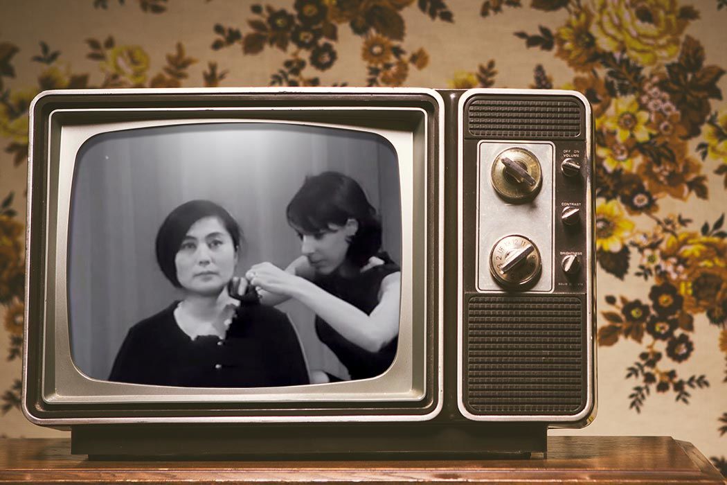 An old television displaying Yoko Ono and a woman fixing her collar