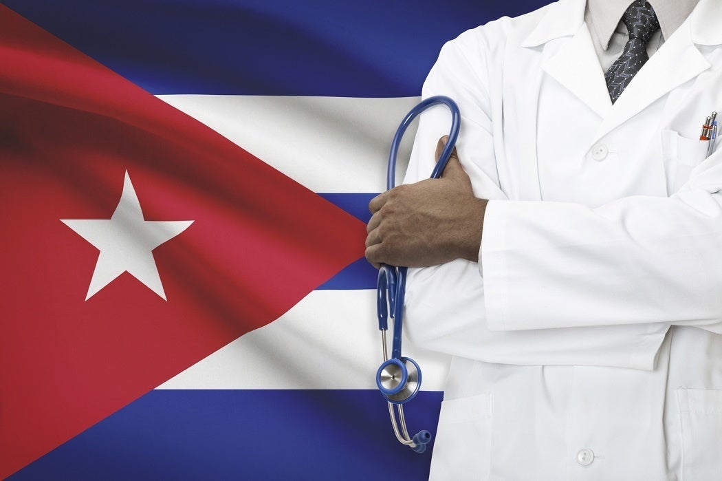 A doctor standing in front of the Cuban flag