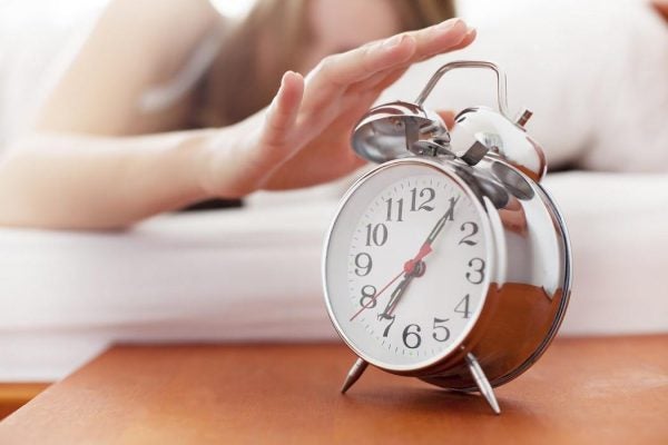 A woman reaches out from bed to silence her alarm clock