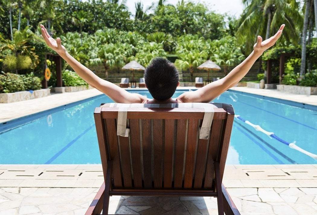 Man sitting on a pool chair with his arms joyfully thrown up