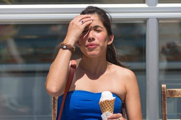 Woman holding her head in one hand and an ice cream cone in the other