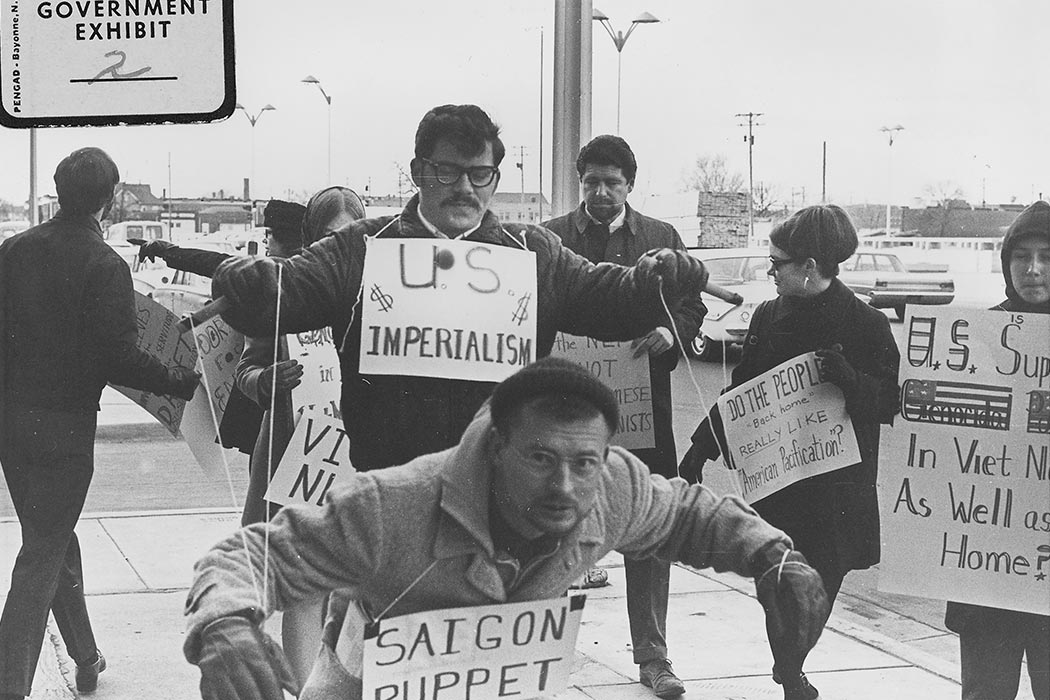 Protesters carry signs and act out "Saigon Puppet" demonstration in front of Wichita City Building.