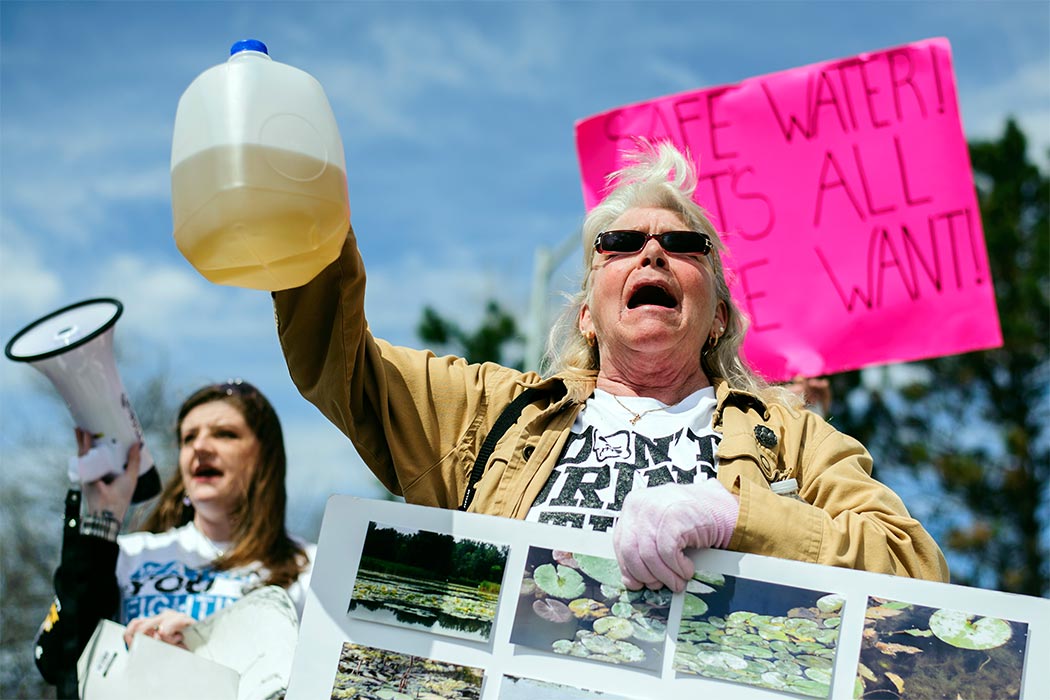 Gladyes Williamson holds up a discolored jug of water and chants along with other protestors outside the Farmers Market downtown on April 25, 2015, which marks the one year anniversary of the City of Flint switching from using Detroit water to Flint River water. Flint residents of all ages gathered outside Flint City Hall, located on S. Saginaw Street, with signs, t-shirts, and megaphones before walking throughout many streets downtown to voice their concerns with the public. (Sam Owens/The Flint Journal-MLive.com via AP)