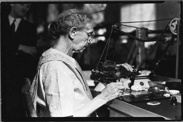 An older female worker uses a machine to make a product