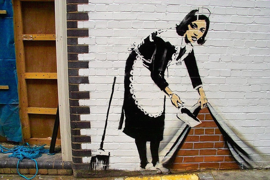 A graffitied maid cleaning up the sidewalk by Banksy