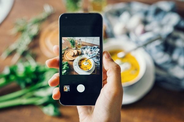 Woman taking photo of pumpkin soup with smartphone