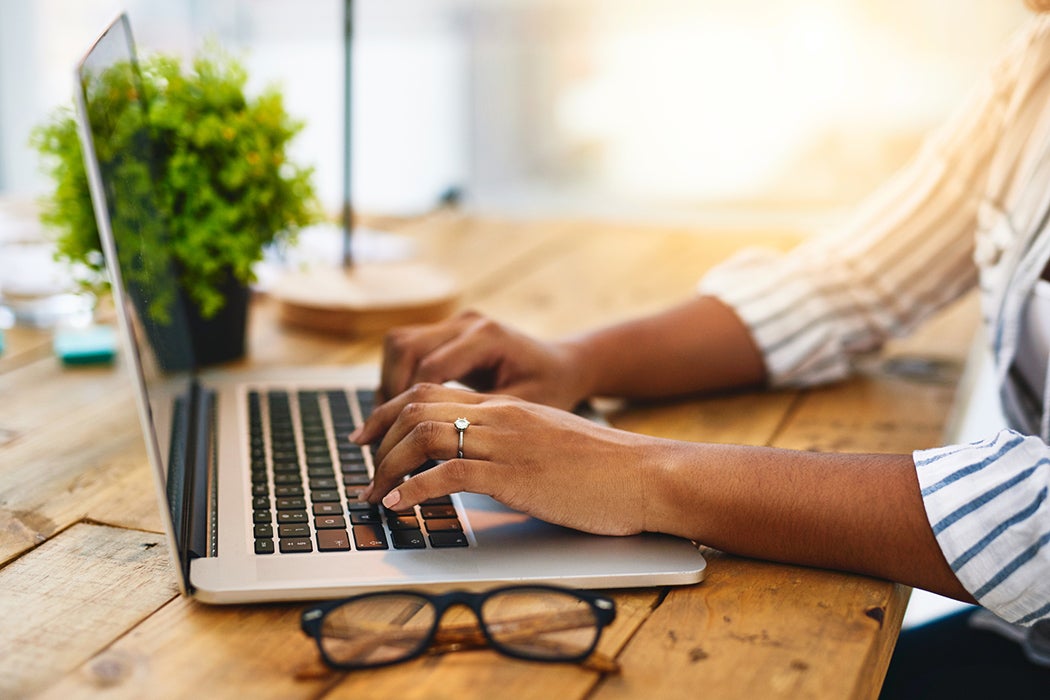 Cropped shot of a woman using her laptop on a wooden table