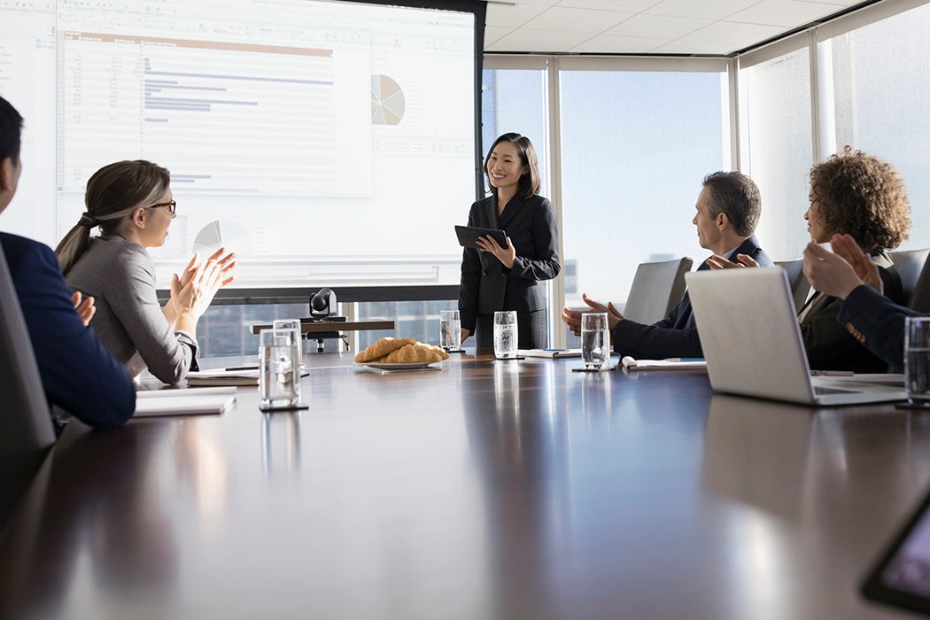 Business people clapping for businesswoman leading presentation in conference room