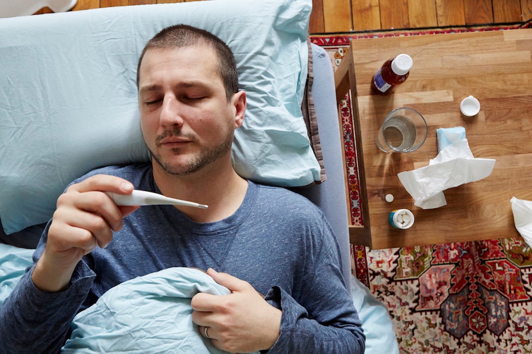 Mid adult man lying in bed looking at thermometer reading