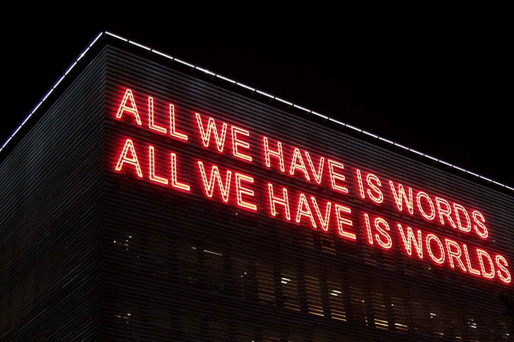 Neon text on the side of a building reads "All we have is words, all we have is worlds."