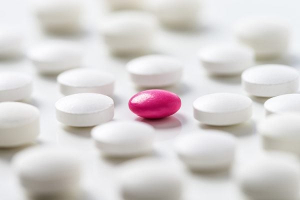 A pink pill on a table amongst white pills.