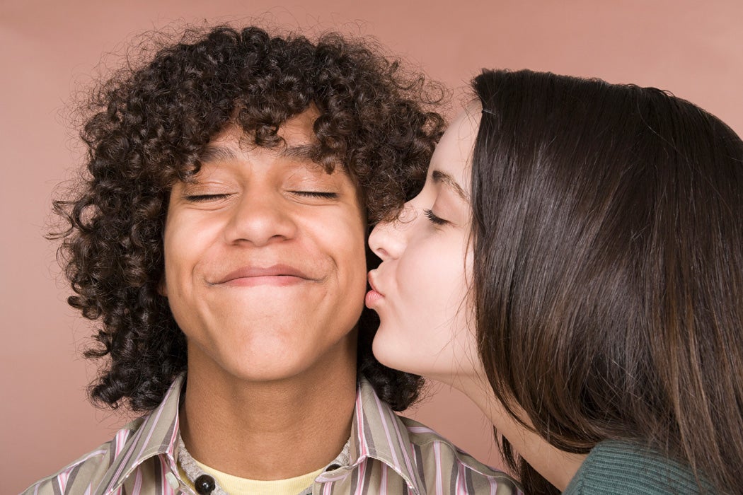 A teenage girl kissing a teenage boy on the cheek