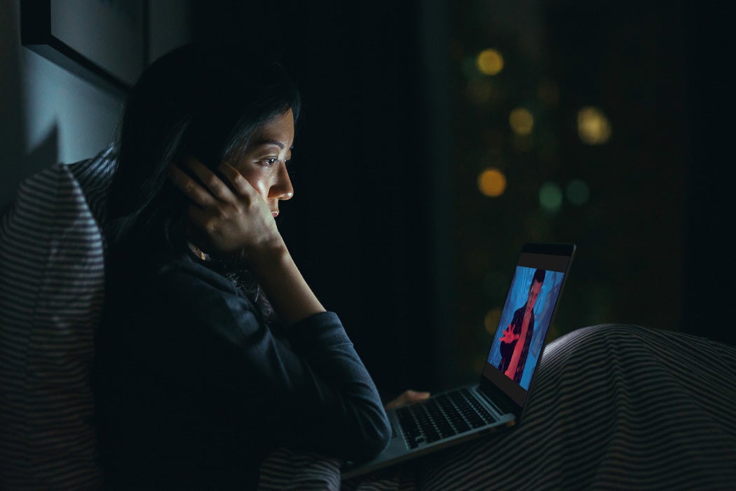 A woman in bed watching Stranger Things on her computer.