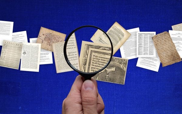 A hand holding a magnifying glass looking at pages with different fonts