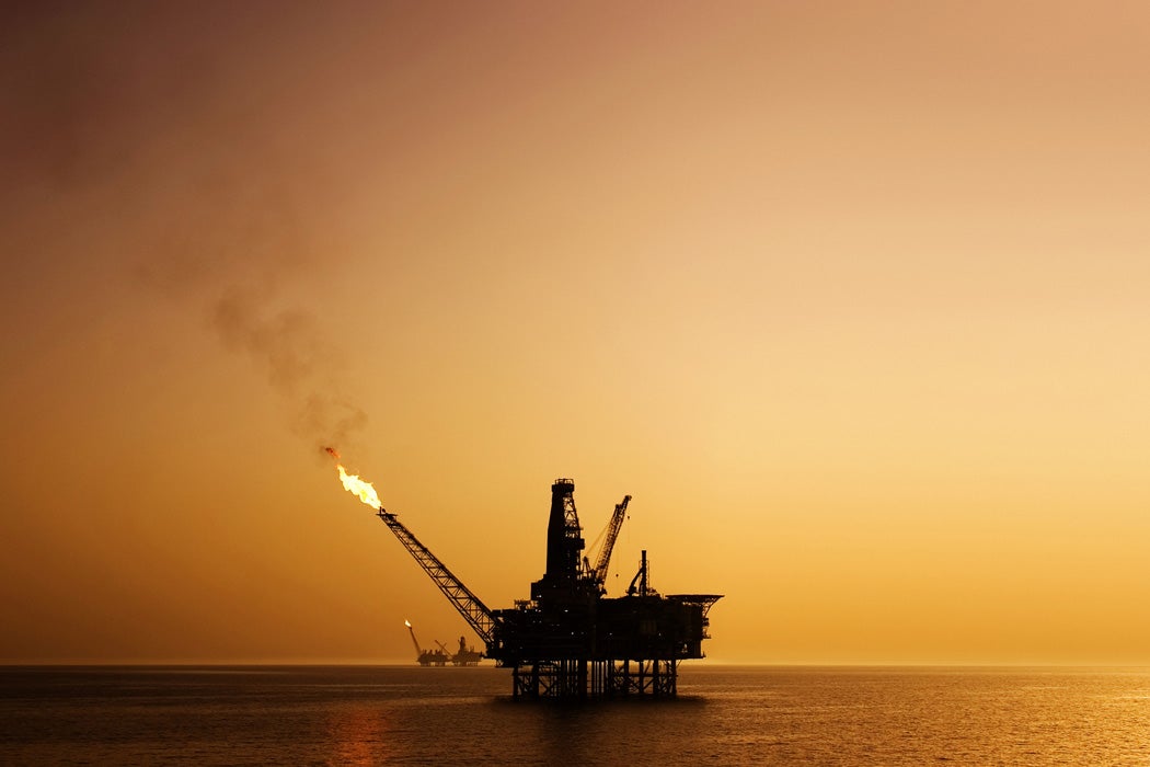 A rig in the ocean with smoke and fire protruding from top