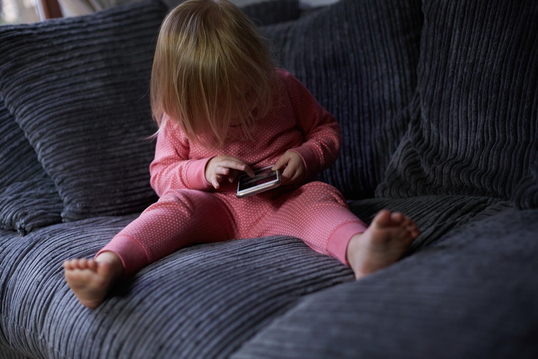 A young girl using a cell phone while sitting on a couch.