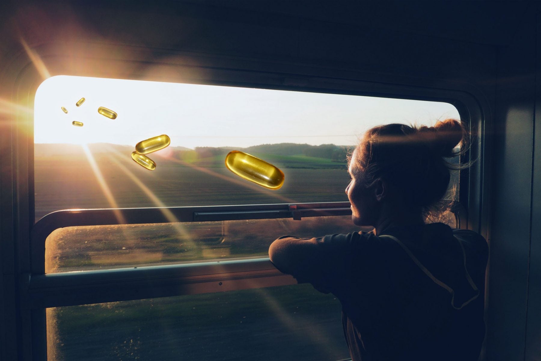 A woman looking out a train window into the sunset with vitamin d pills approaching
