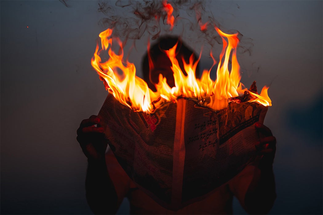 A person holding a newspaper on fire