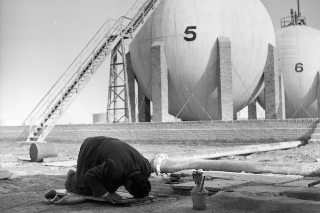Photograph: A Mohammadan praying towards Mecca when the Miezzin calls from a nearby mosque, with a Butane Gas reservoir in the background. circa 1950