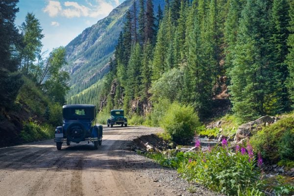 Classic cars drive along dirt road in the mountains