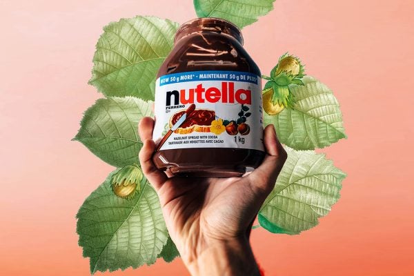 A hand holding a jar of Nutella in front of an illustrated hazelnut plant
