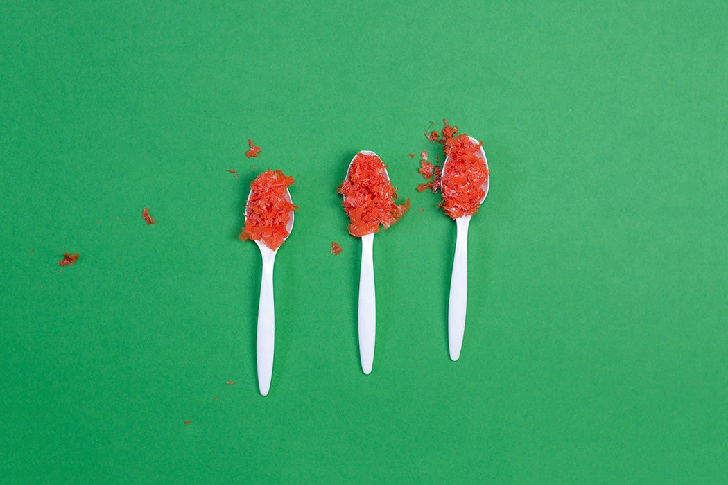 Three spoonfuls of red microplastic on a green background.