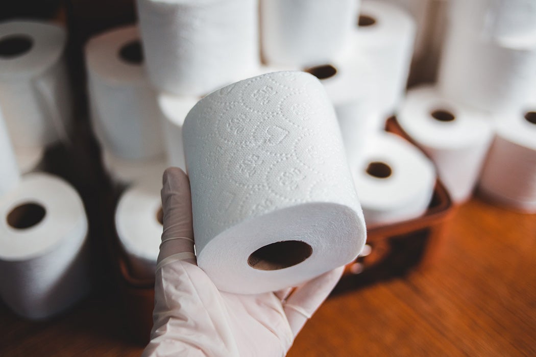 A gloved hand holding a roll of toilet paper
