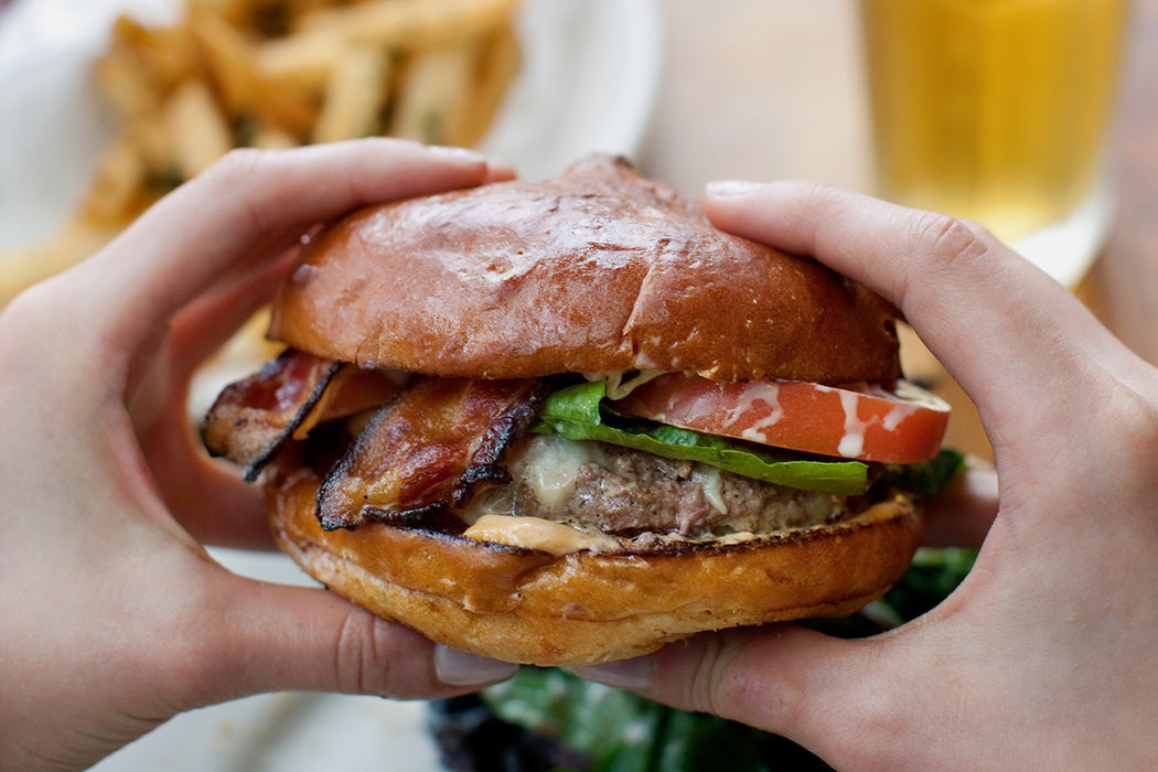 Two hands hold a scrumptious looking bacon cheeseburger.