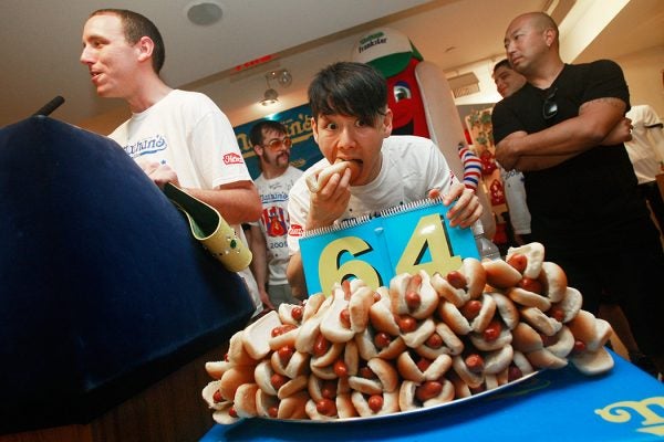 Former champion Takeru Kobayashi bites a hot dog as reigning champion Joey Chestnut (L) speaks at the Nathan's Famous Fourth of July International Hot Dog Eating Contest official weigh-in ceremony July 2, 2009 in New York City