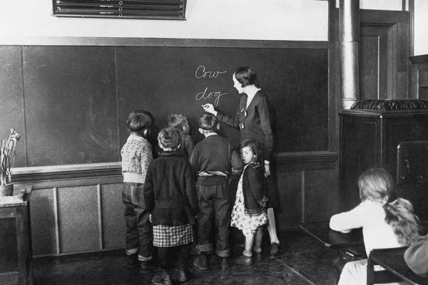 A teacher teaches her young pupils how to spell, 1930.