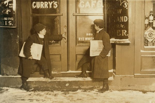 Two boys selling newspapers outside of a saloon