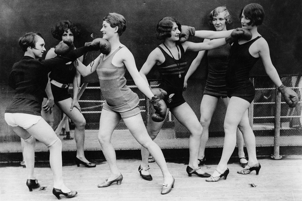 Photograph: Female referees look on as two pairs of young women simulate boxing in a ring, 1931.