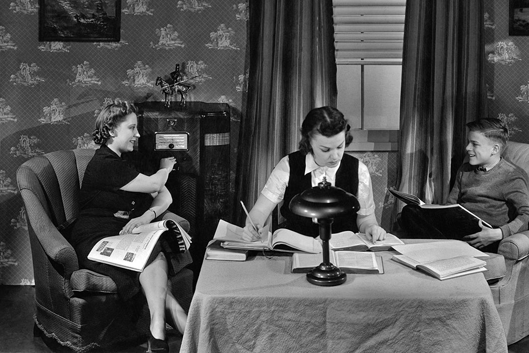 A girl and boy doing homework as a woman listens to the radio in the 1940's