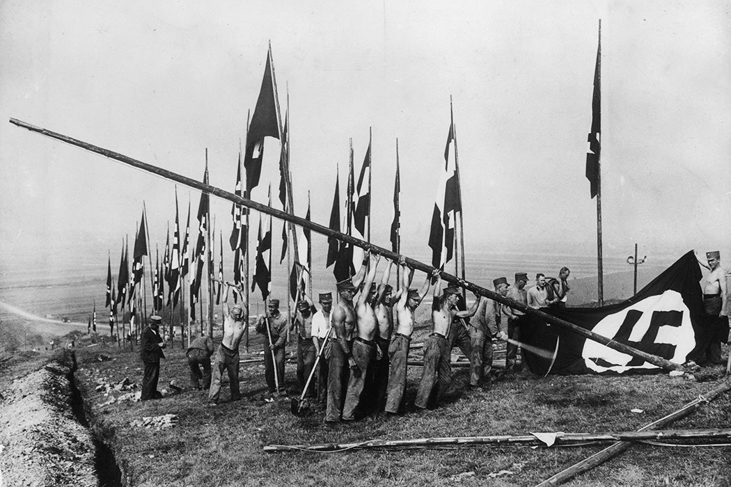 Barechested workers erect a Nazi flag on a hill at Buckeberg in preparation for a Harvest Festival.