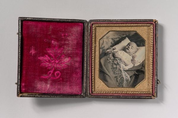 A daguerreotype of a postmortem baby, partially covered by a flowered shawl