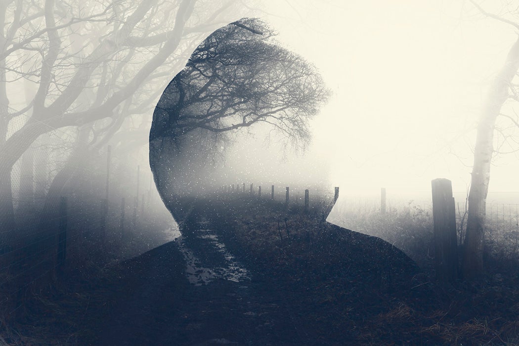 A double exposure of a spooky half transparent hooded figure layered over a foggy path in the countryside